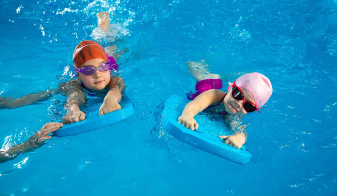 Two,Little,Girls,Learning,How,To,Swim,In,Swimming,Pool